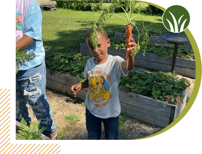 A young boy holding up an orange carrot.