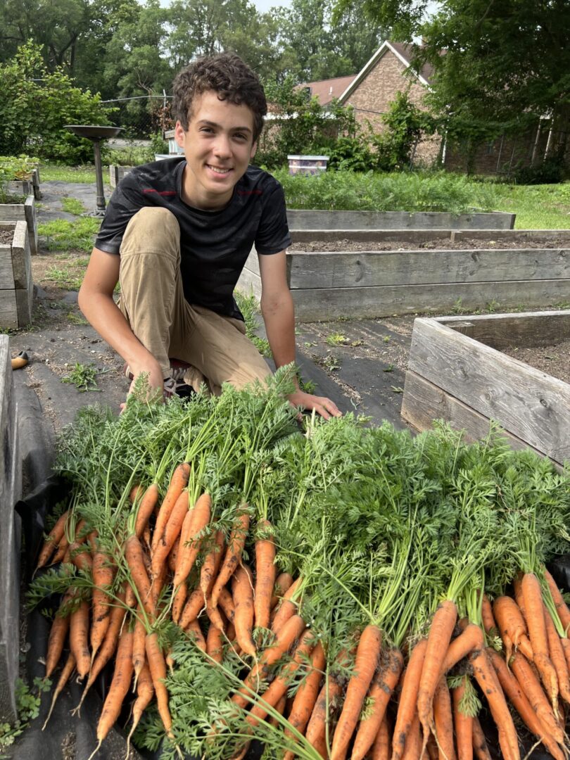 A man kneeling down next to a pile of carrots.